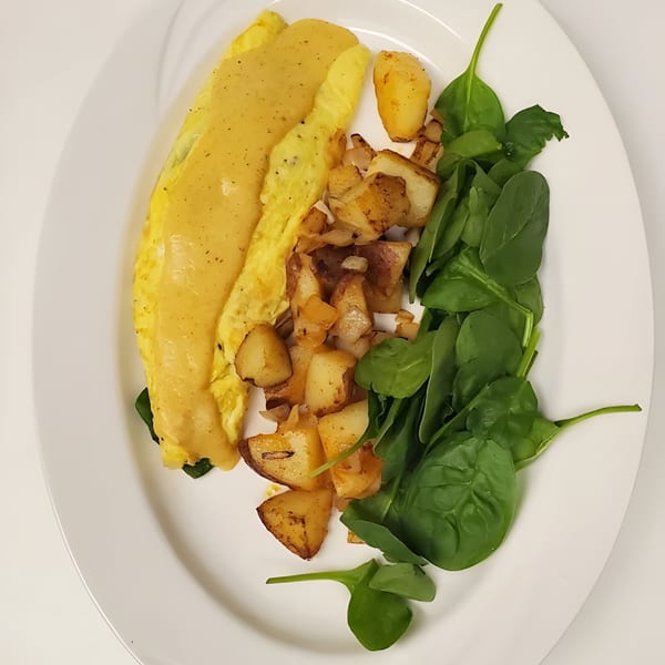 A breakfast plate with a yellow omelet, home fries, and fresh spinach on a white plate.