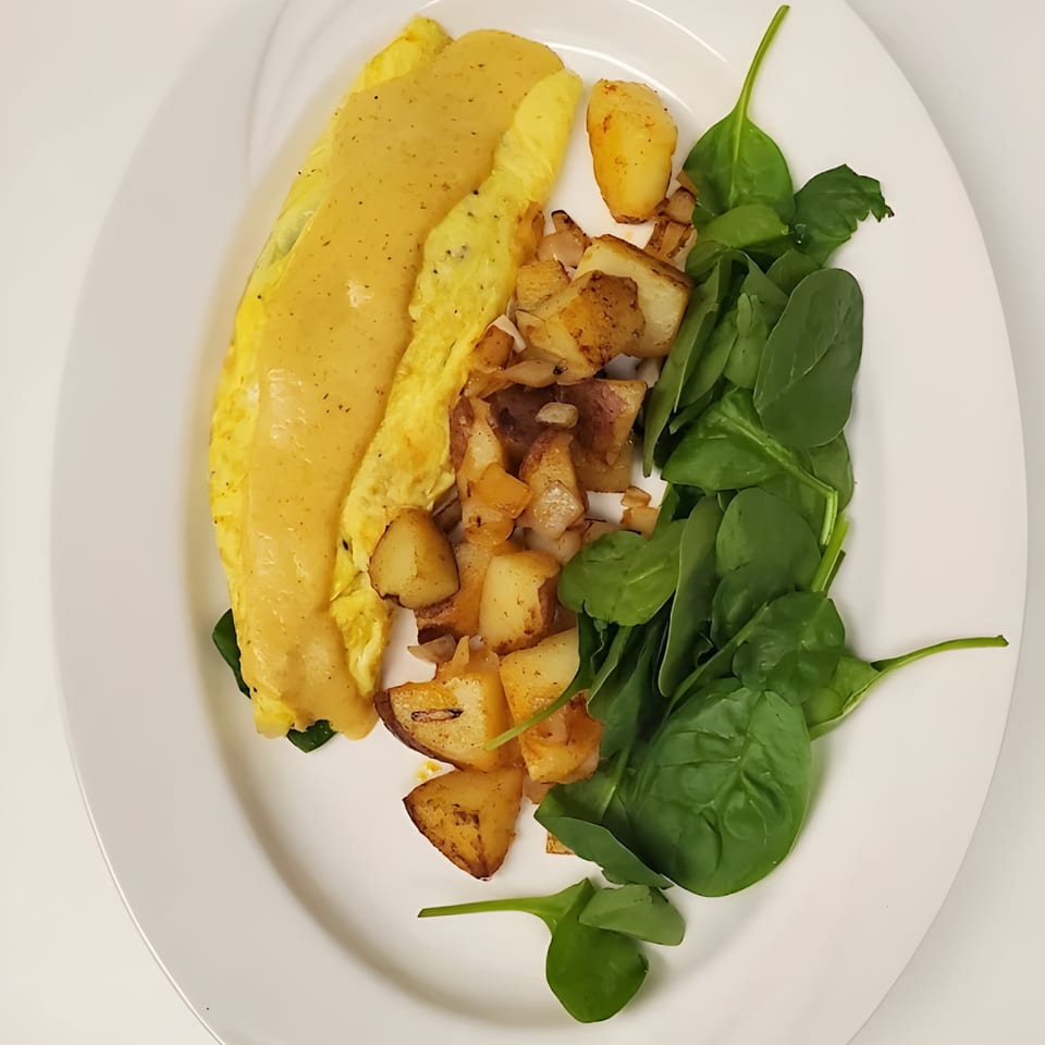 A breakfast plate with a yellow omelet, home fries, and fresh spinach on a white plate.