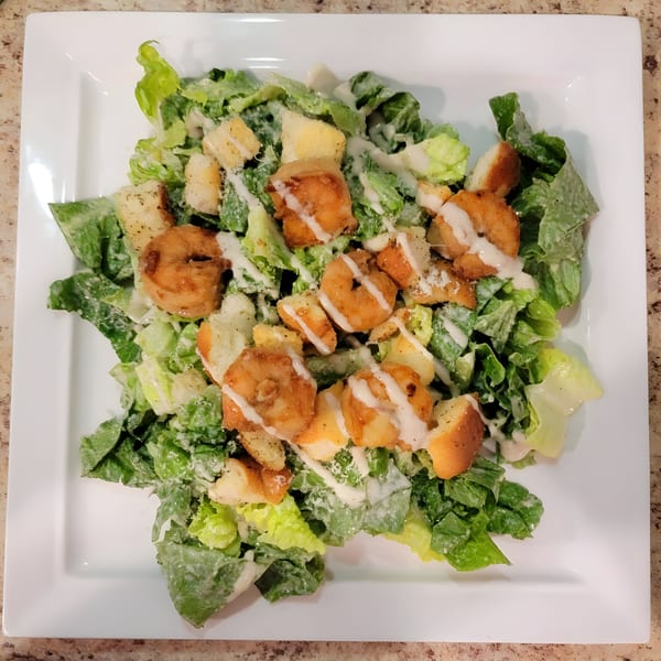 A Caesar salad with crispy fried shrimp, croutons, and creamy dressing on a white plate.