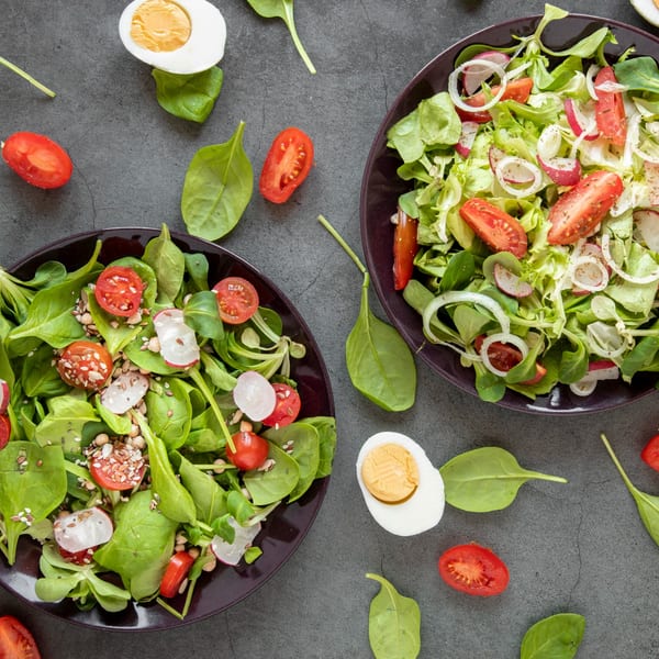 Two vibrant salads with greens, tomatoes, radishes, and onions, with scattered ingredients and boiled eggs.