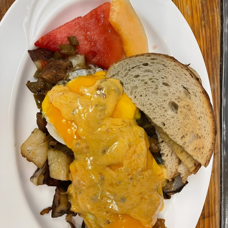 Breakfast plate with eggs benedict, home fries, toast, watermelon, and cantaloupe.