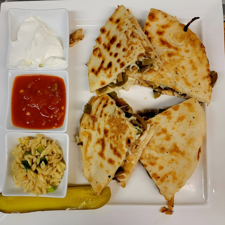 Four quesadilla slices with melted cheese and green peppers, served with sour cream, salsa, orzo, and a pickle.